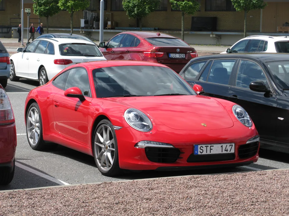 Guards Red Porsche 911 Carrera (991.1) coupé parked in a Swedish car park, three-quarter front view