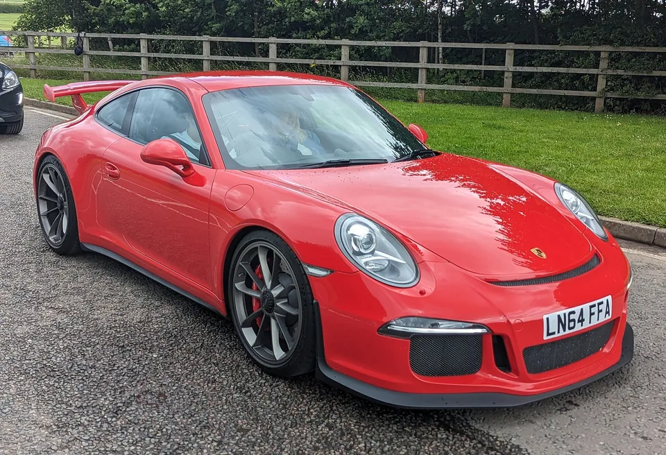 Guards Red Porsche 911 GT3 (991.1) coupé on a gravel drive, three-quarter front view