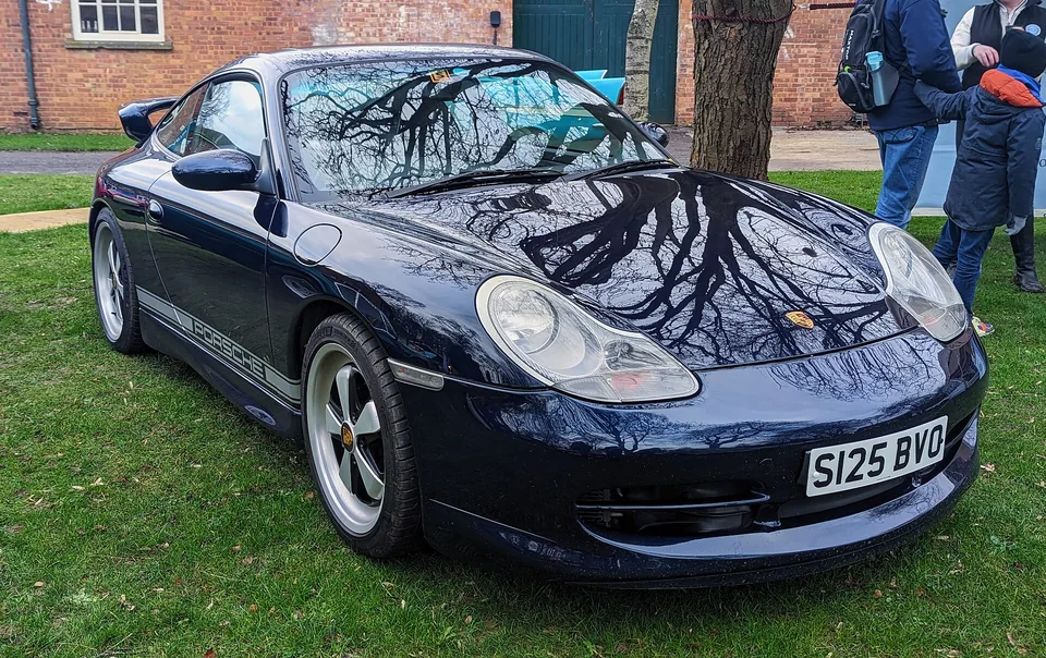 Midnight Blue Porsche 911 Carrera (996.1) coupé on grass at Bicester Heritage, three-quarter front view