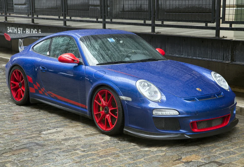 Aqua Blue 2011 Porsche 911 GT3 RS (997.2) with red wheels, red mirrors and RS graphics on cobblestones in Brooklyn, three-quarter front view